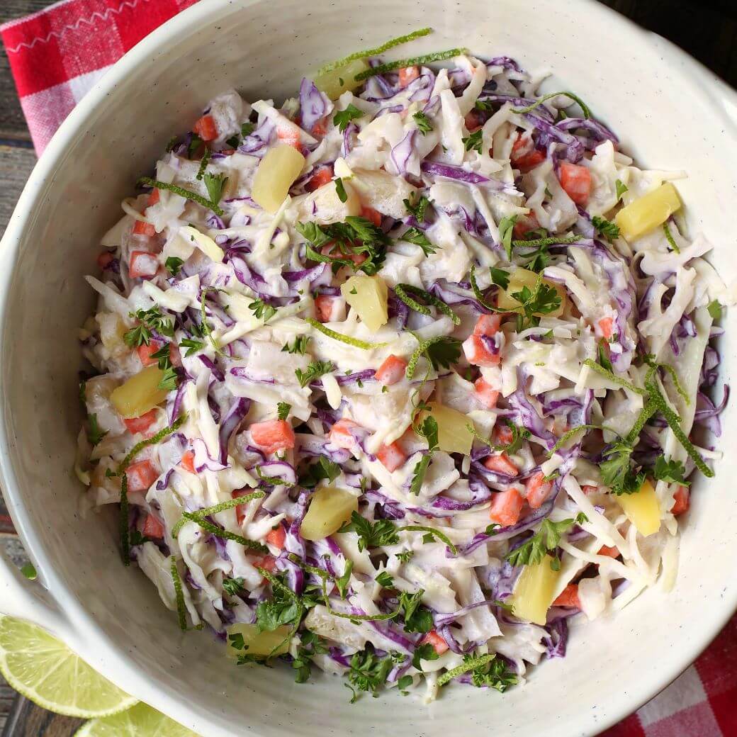A multicoloured coleslaw with pineapple and lime in a white bowl.