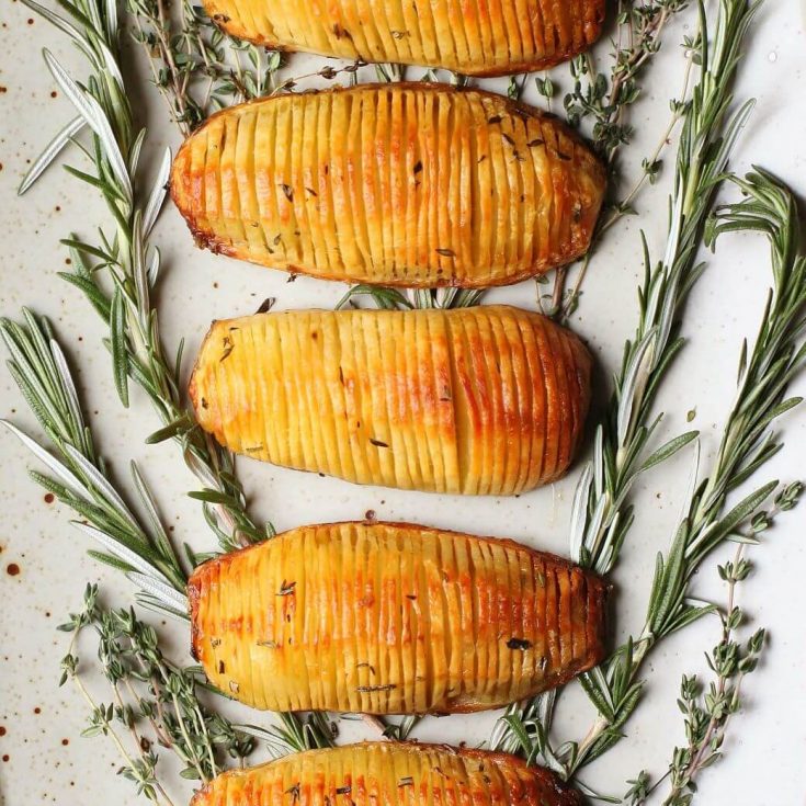 Crispy Herbed Hasselback Potatoes - Five crispy golden potatoes rest on a bed of fresh herbs.