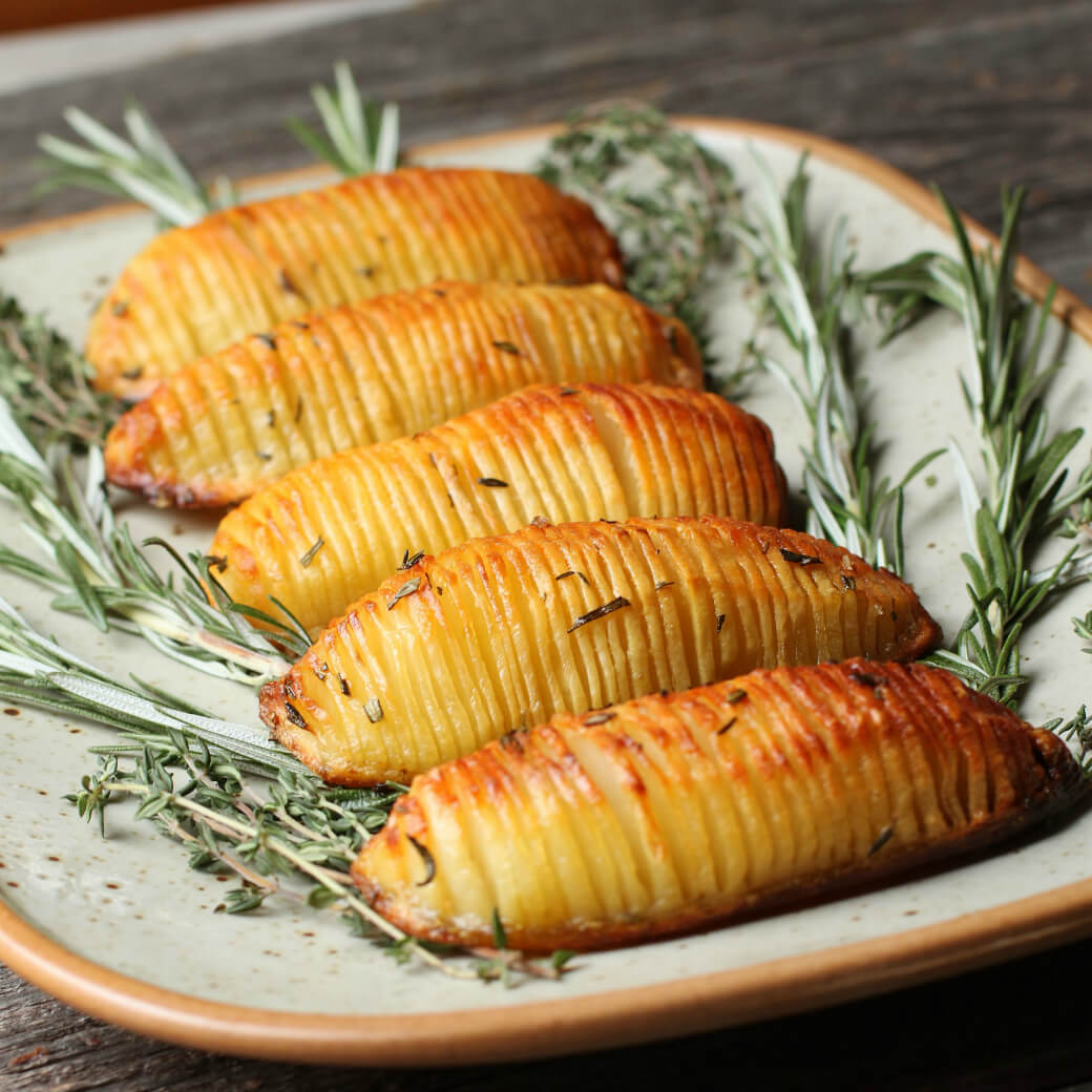 Crispy Herbed Hasselback Potatoes - Five crispy golden potatoes rest on a bed of fresh herbs.