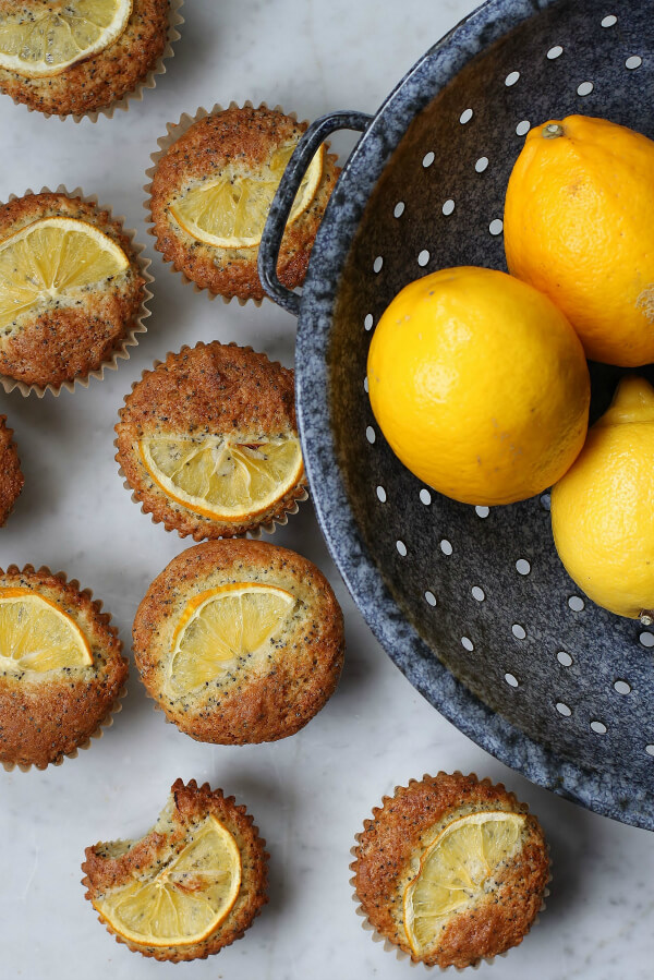 Bright yellow Meyer Lemons in a blue colander surrounded by muffins.