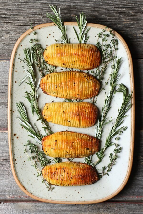 Crispy Herbed Hasselback Potatoes - Five crispy golden potatoes rest on a bed of fresh herbs.