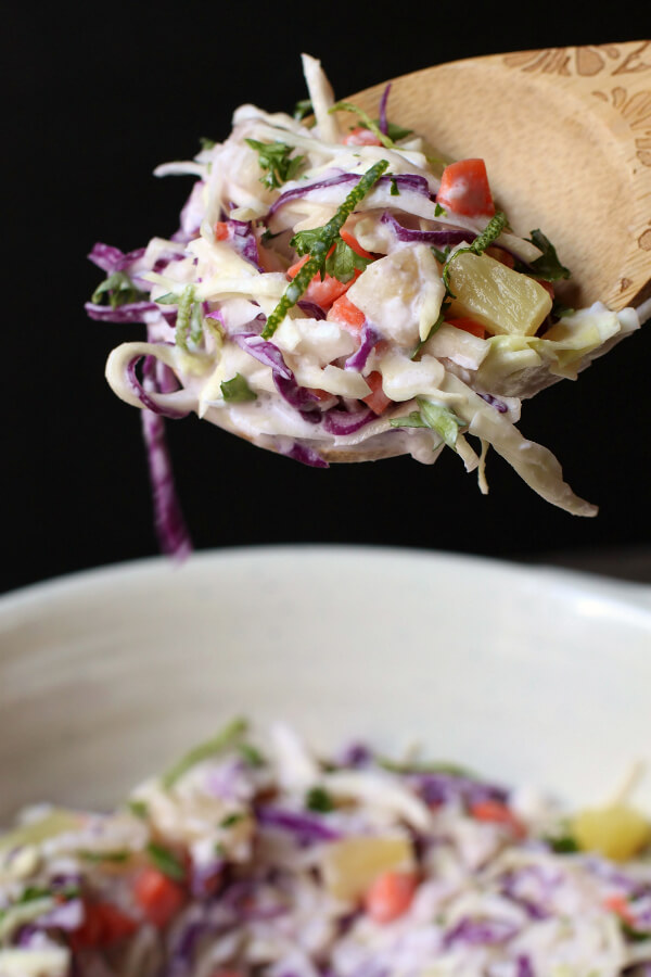 A close up of a multicoloured coleslaw with pineapple and lime on a wooden spoon.