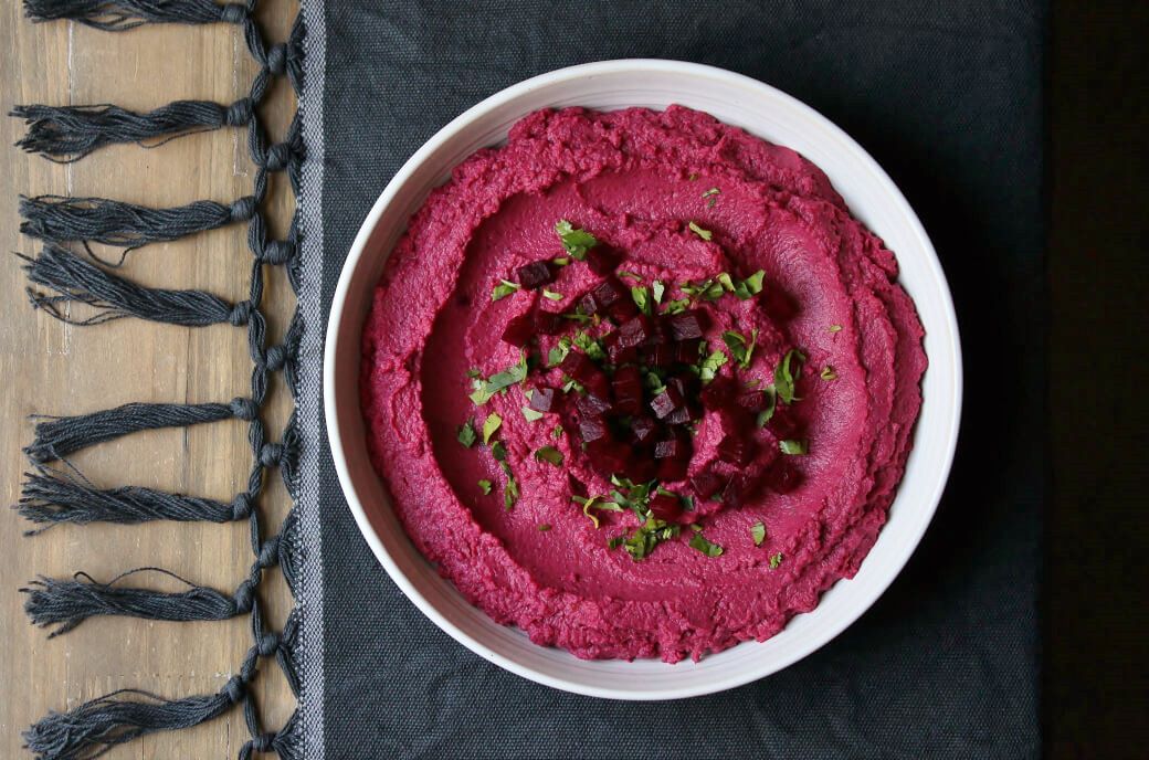 Baharat Roasted Beet Hummus - A bowl of brightly coloured pink hummus garnished with olive oil, beet cubes, and parsley.