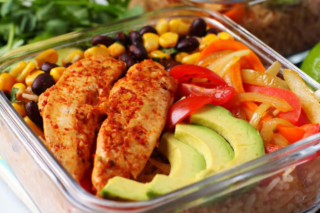 Simply Delicious Chicken Burrito Bowl - a square glass fridge container filled with chicken, rice, peppers, avocado, corn and beans.