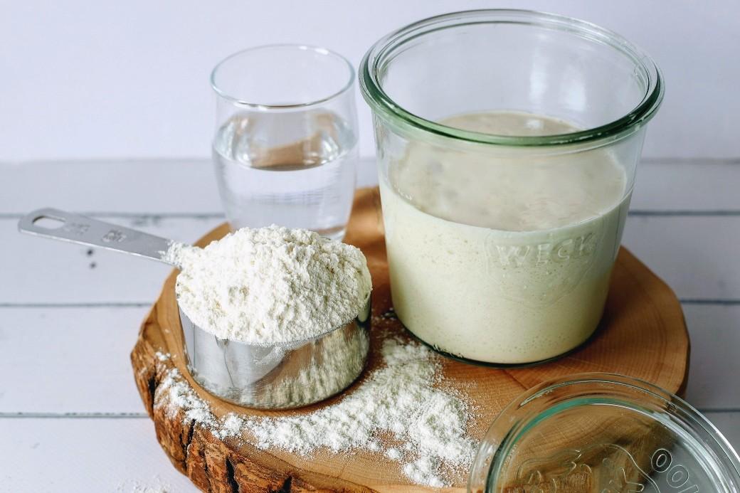 How to Make Sourdough Starter - sourdough starter in a glass jar surrounded by measuring cup of flour and jar of water.