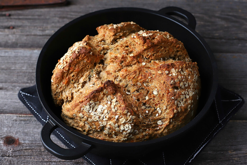 Cheesy Cheddar Stout Soda Bread - a golden baked soda bread in a cast iron pan on a wooden background