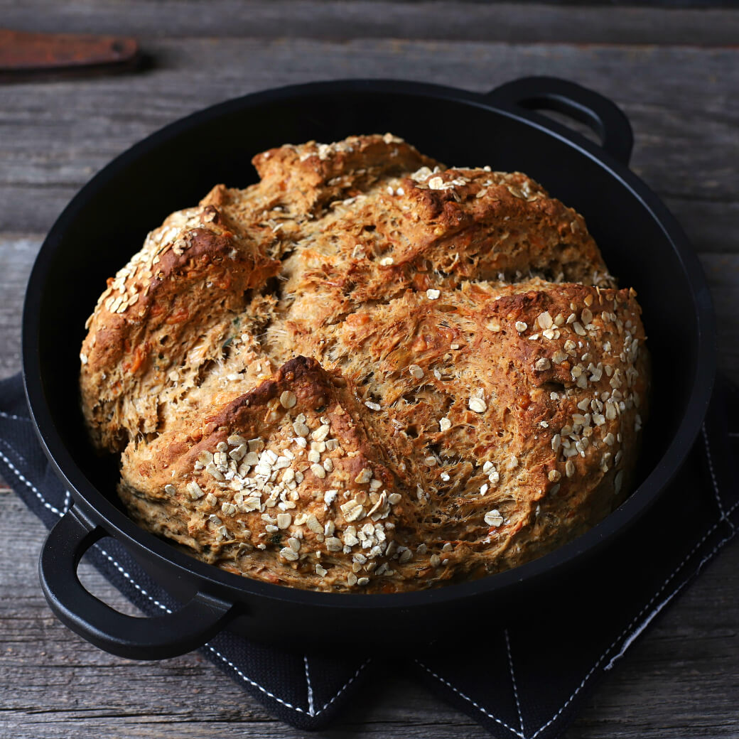 Cheesy Cheddar Stout Soda Bread - a golden baked soda bread in a cast iron pan on a wooden background