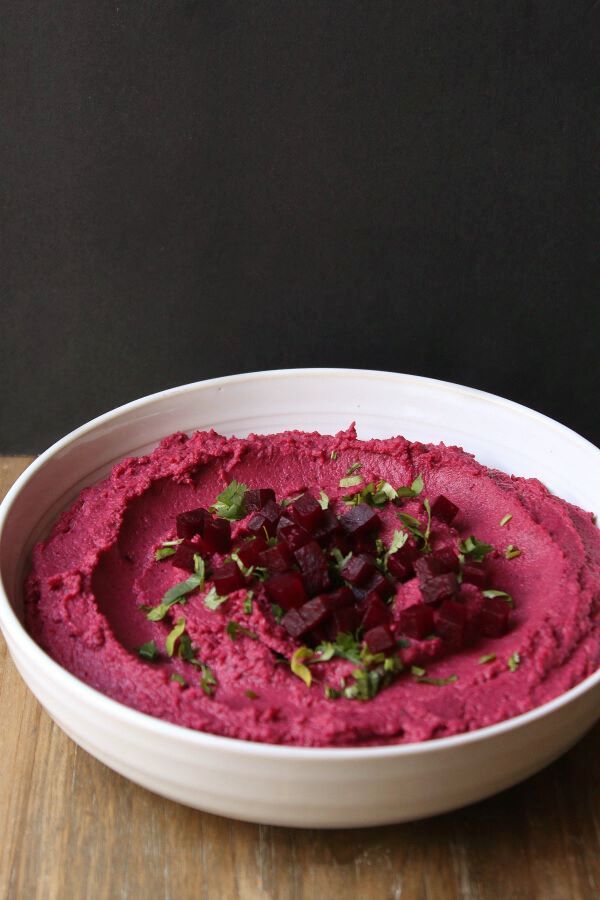 Baharat Roasted Beet Hummus - A bowl of brightly coloured pink hummus garnished with olive oil, beet cubes, and parsley.