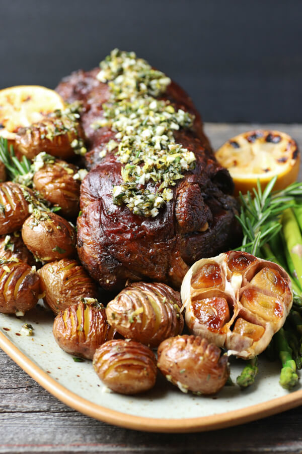 A platter filled with a boneless roasted leg of lamb, potatoes, asparagus, roaster garlic, and charred lemon.