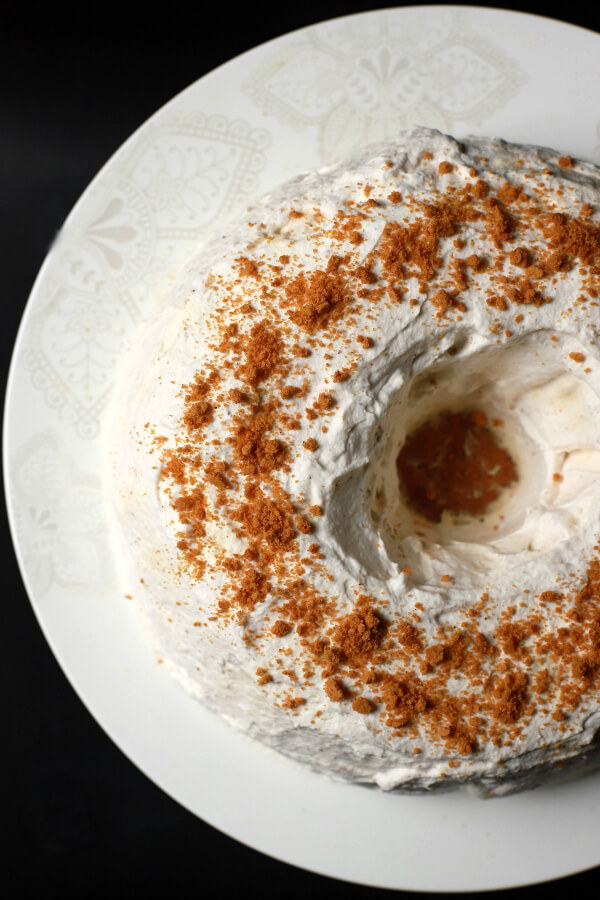 Top view of a white circular cake topped with ginger crumbs against a black background.