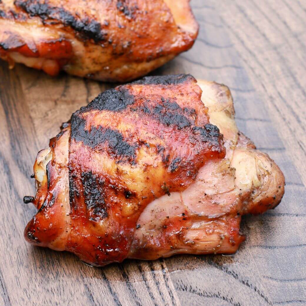 One perfectly smoked and grilled chicken thigh on dark wooden board.