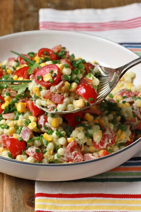 Smoked Corn Bacon Avocado Pasta Salad is a bright and cheerful salad containing red grape tomatoes, corn, bacon, cilantro, and pearl couscous in a white bowl.
