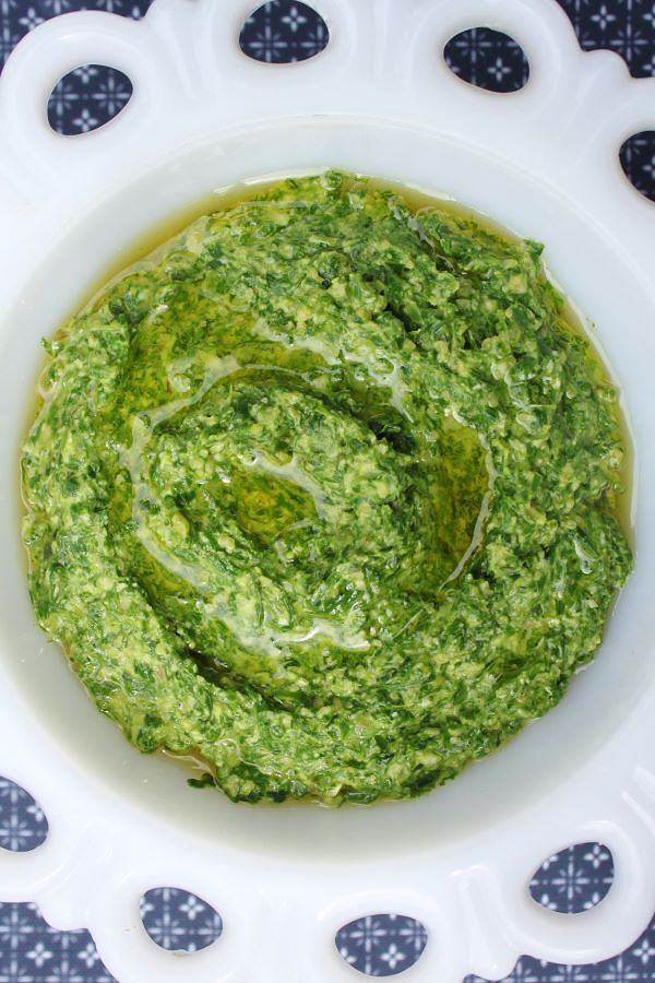 A scalloped white bowl filled with vibrant green pesto surrounded by ramp leaves.