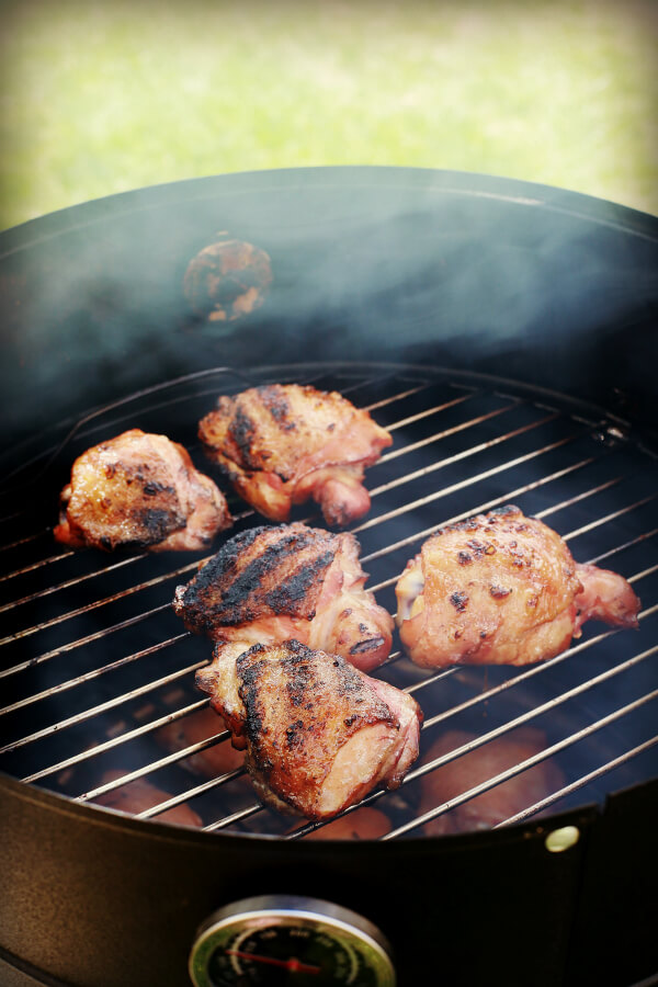 Five chicken thighs on a barbecue grill. with smoke rising.