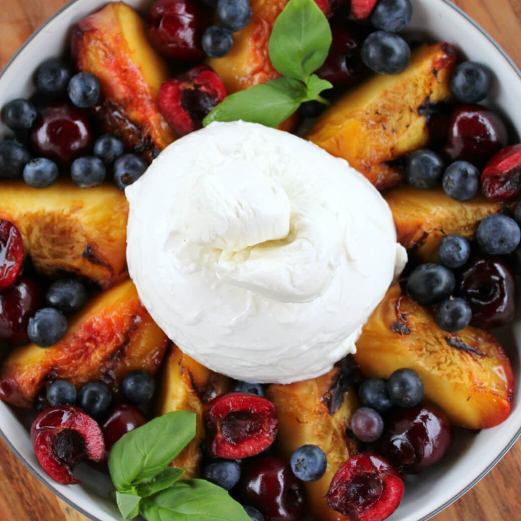a bowl of colourful fruit topped with fresh cheese with a wood background