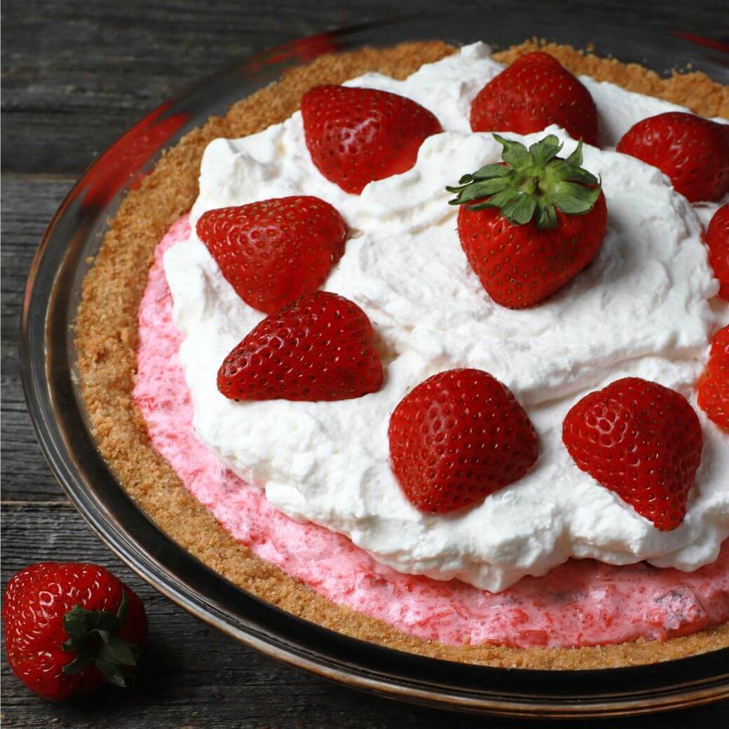 A pink pie in a graham crust topped with strawberries and whipped cream.