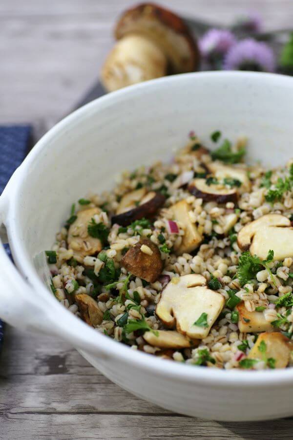 A white bowl filled with barley, fresh herbs, and porcini mushrooms.