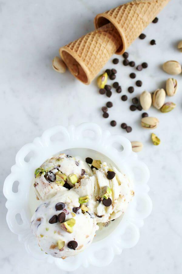 A white dish holds three scoops of ice cream dotted with chocolate chips and pistachios.