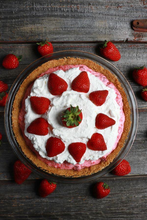 A pink rhubarb strawberry pie in a graham crust topped with strawberries and whipped cream.