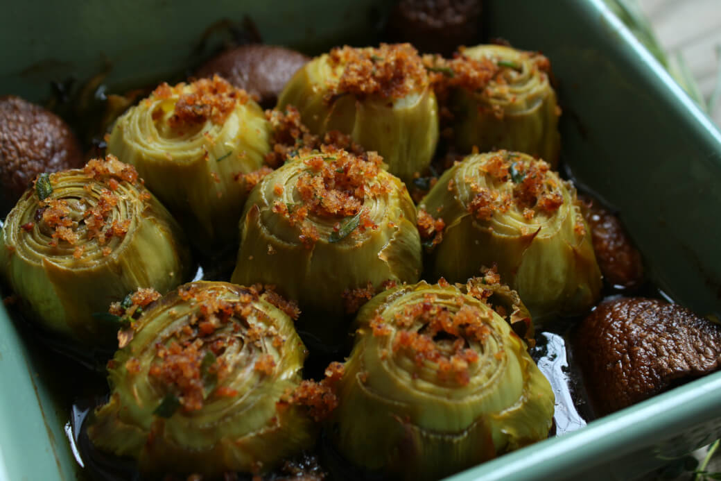 A baking dish full of Roasted Baby Artichokes topped with olive oil, bread crumbs,and Rosemary.