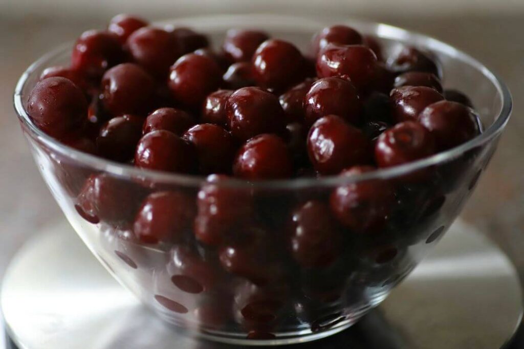 A clear glass bowl full of sour cherries.