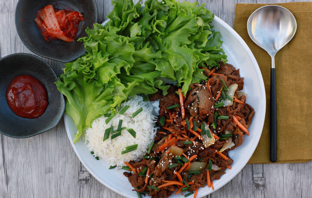 A white plate filled with caramelized beef, rice and green lettuce. 