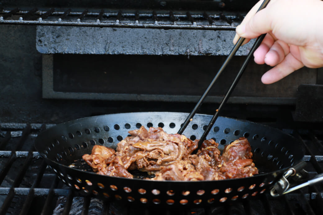 A pair of chopsticks being used to quickly grill marinated beef in a grilling basket.