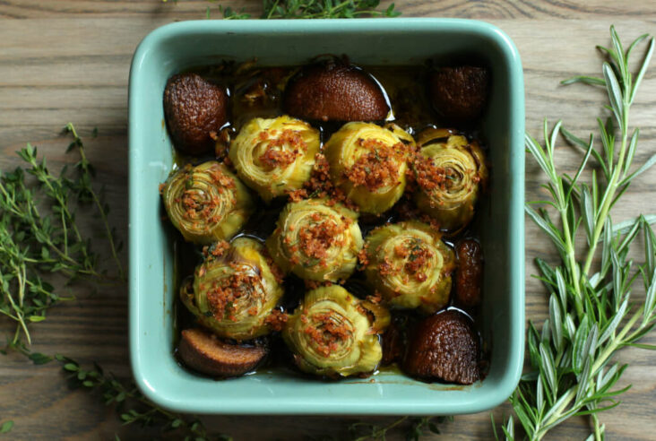 A baking dish full of Roasted Baby Artichokes topped with olive oil, bread crumbs,and Rosemary.