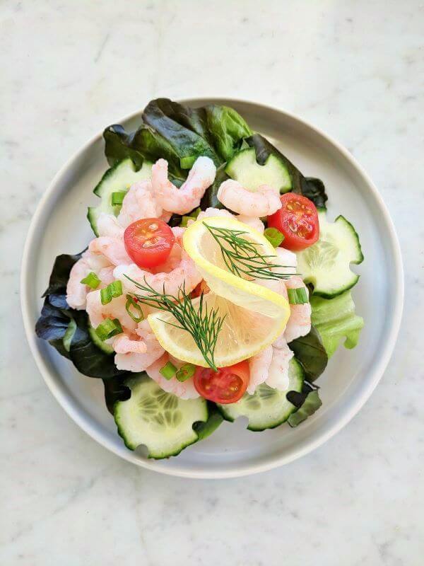 Open faced shrimp sandwich piled high with lettuce, cucumbers, cherry tomatoes, shrimp, lemon, and dill.