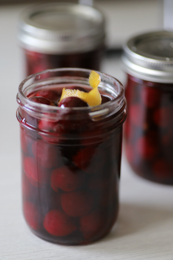 A jar full of ready to be canned cocktail cherries topped with a lemon peel.