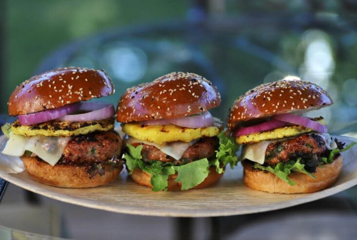 Three Pork Burgers loaded with red onions, grilled pineapple, melted cheese, pork patty and lettuce.