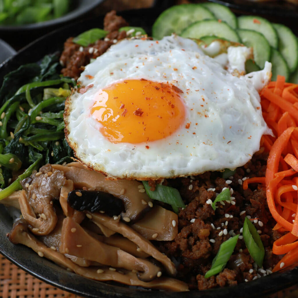 A bowl of vegetables and ground beef topped with an egg.