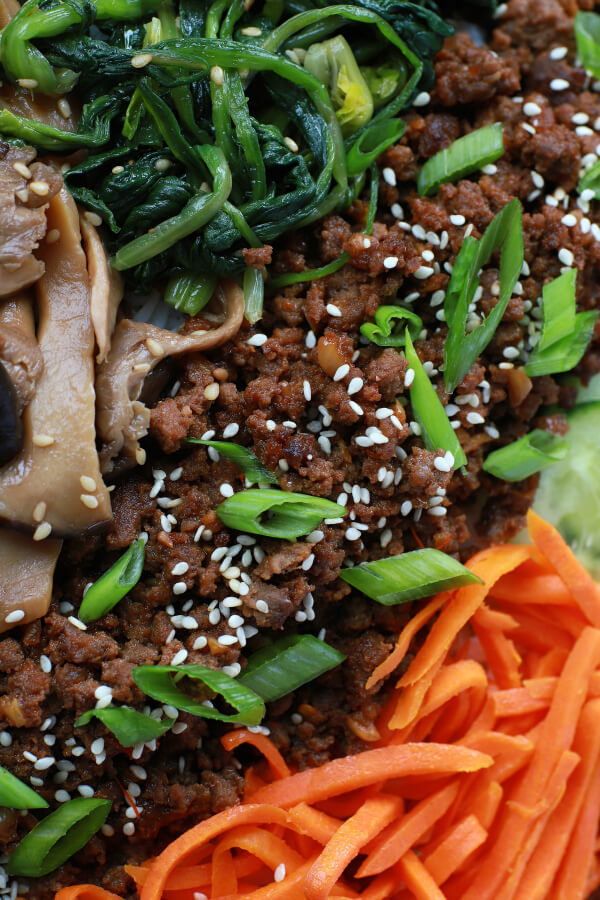 Close up of spicy ground beef surrounded by vegetables and topped with sesame seeds and green onions.