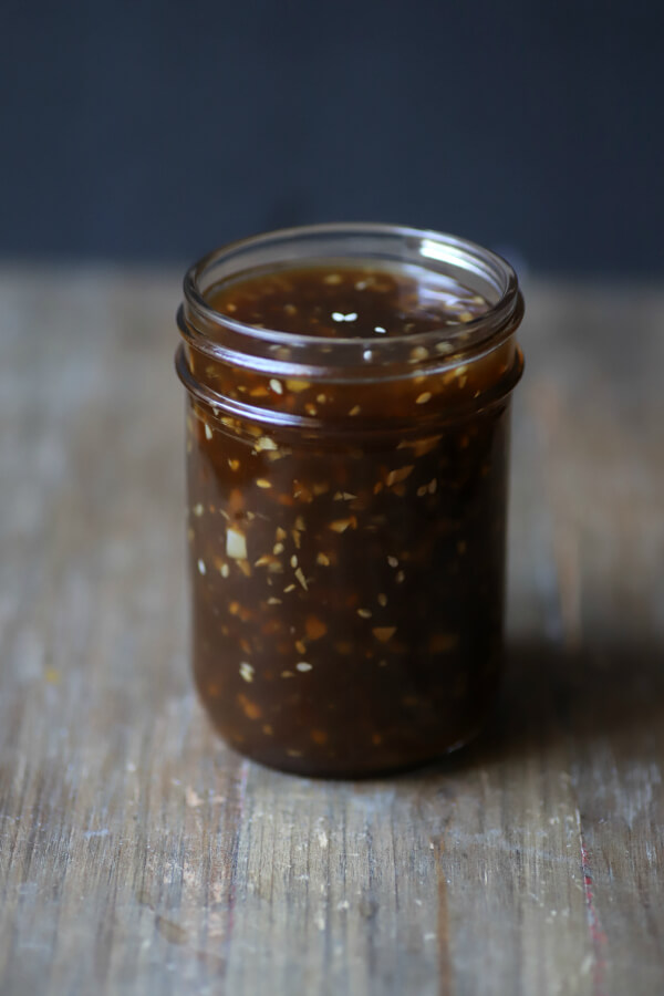 A jar holds brown Honey Teriyaki Sauce containing chunks of garlic and ginger.