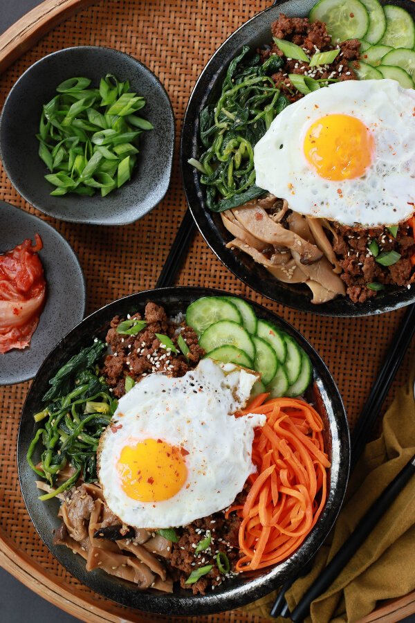 Two bowls of vegetables and ground beef topped with an egg.