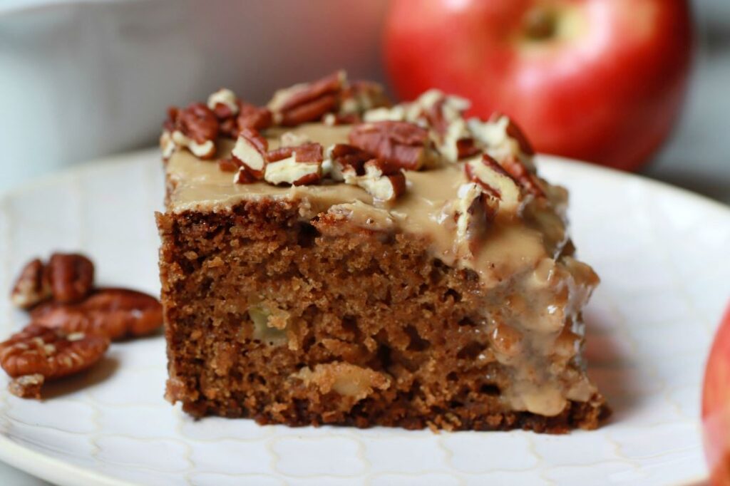 A slice of chunky apple cake topped with brown sugar glaze and pecans.