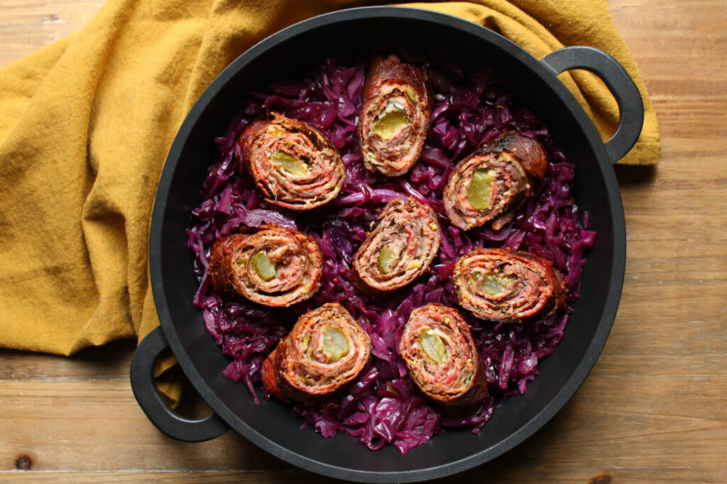 Beef and bacon rolled around a pickle sitting on a bed of red cabbage.