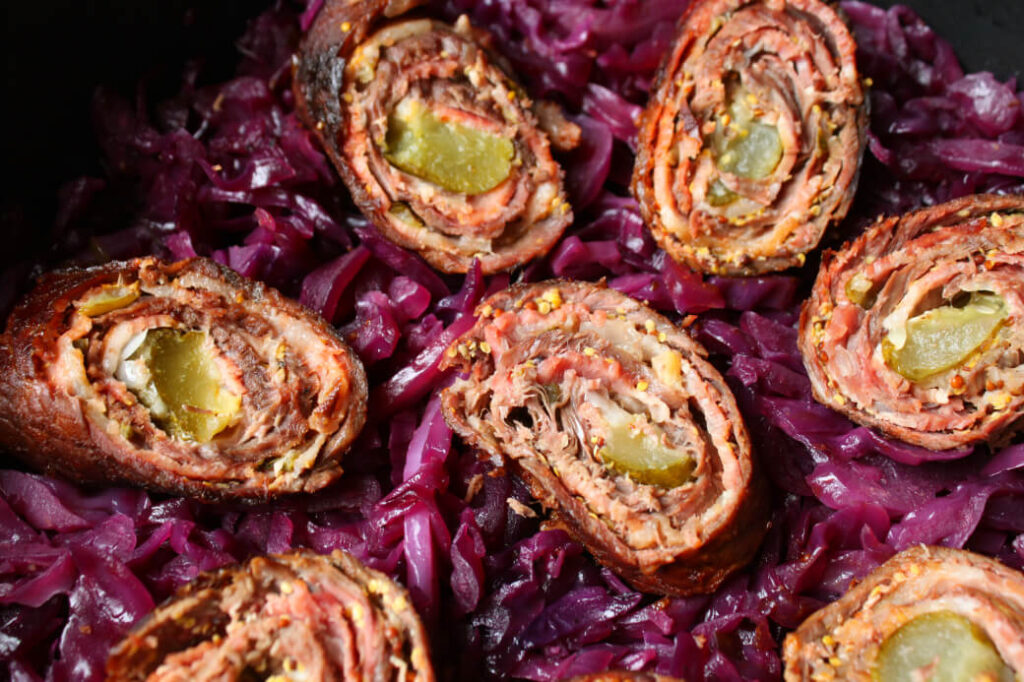 Beef and bacon rolled around a pickle sitting on a bed of red cabbage.