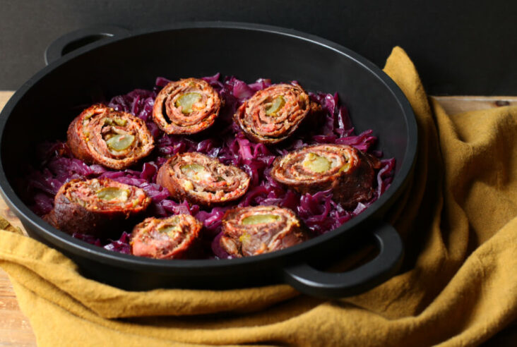 Beef and bacon rolled around a pickle sitting on a bed of red cabbage.