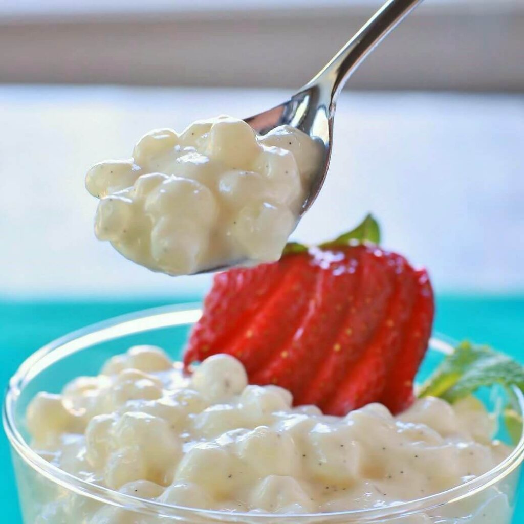 A spoon filled with tapioca pudding hovers over a bowl of the creamy dessert.