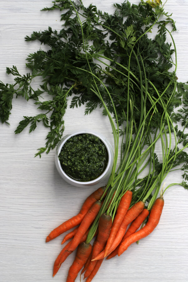 Green pesto in white bowl surrounded by whole carrots.