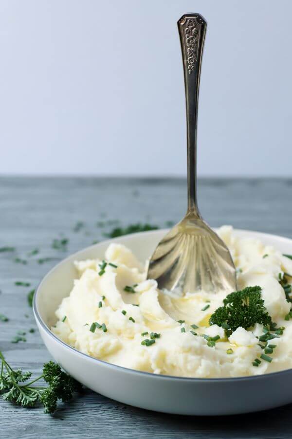 A vintage silver spoon standing up straight in a bowl of mashed potatoes.