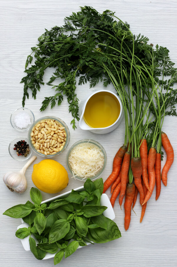 Ingredients needed to make carrot top pesto including carrot greens, pine nuts, olive oil, Parmesan cheese, basil, lemon, and garlic.