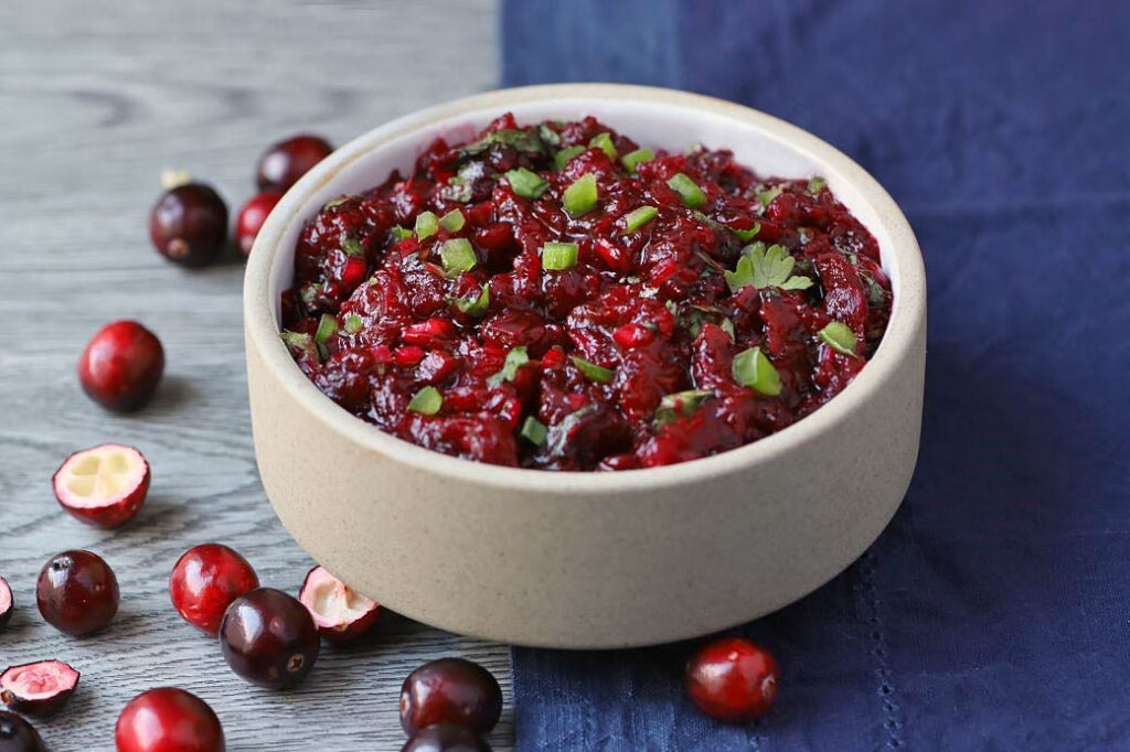 A white bowl filled with bright red cranberry salsa topped with fresh chopped cilantro.