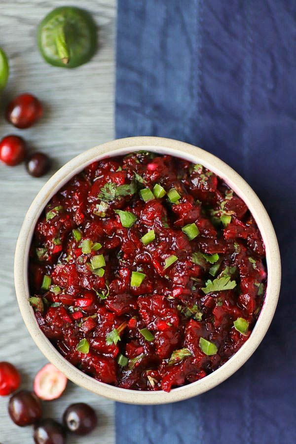 A white bowl filled with bright red cranberry salsa topped with fresh chopped cilantro.