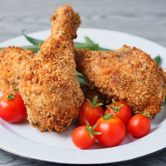Three pieces of golden crispy oven baked chicken on a white plate with green beans and cherry tomatoes.