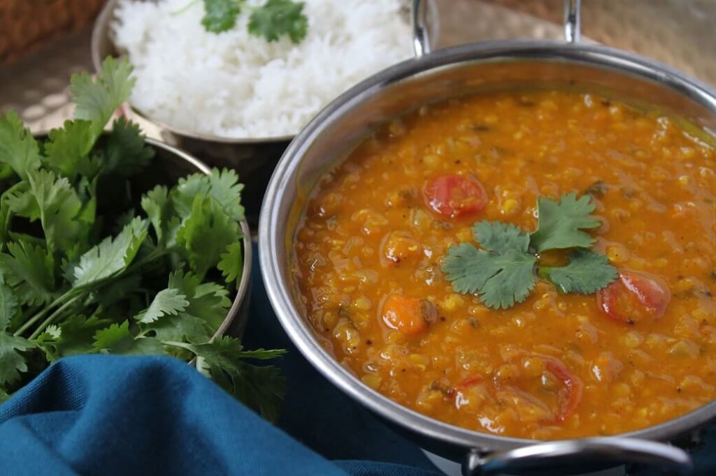 A silver serving bowl filled with red lentil daal and vegetables.