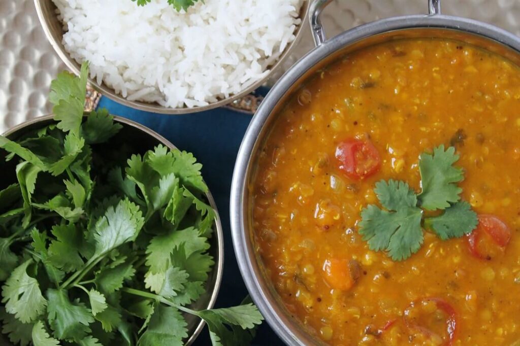 A silver serving bowl filled with red lentil daal and vegetables.