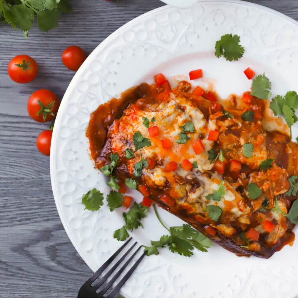 A white plate containing cheesy baked enchiladas topped with diced peppers and cilantro.