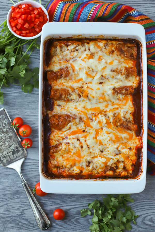 A white baking pan filled with baked cheesy enchiladas and red sauce.